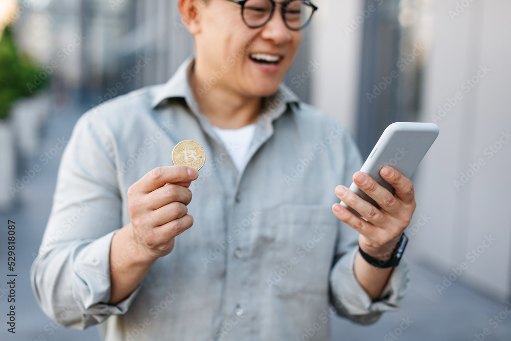 Online trading. Happy asian man holding golden bitcoin and smartphone, middle aged male earning cryptocurrency Online trading. Happy asian man holding golden bitcoin and smartphone, middle aged male earning cryptocurrency