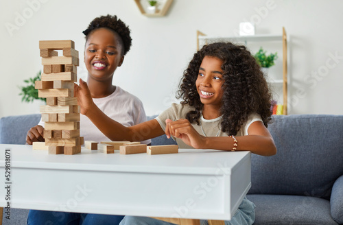 Fotografia Happy little African American girl with mom taking blocks from tumble tower has fun enjoying communication with parent and playing board game sits on sofa in home environment