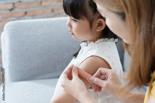 Asian mother attaching the plaster adhesive  bandage onto her daugther arm.