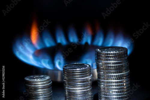 A stack of metal coins on the background of a burning gas burner, dark tones, a place for text, copy space. Concept: rising gas and energy prices, increased rent.