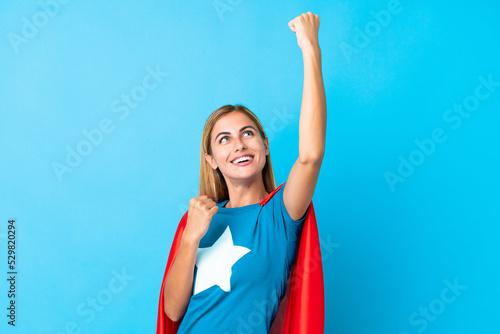 Bild auf Leinwand Blonde woman over isolated background in superhero costume and celebrating a vic