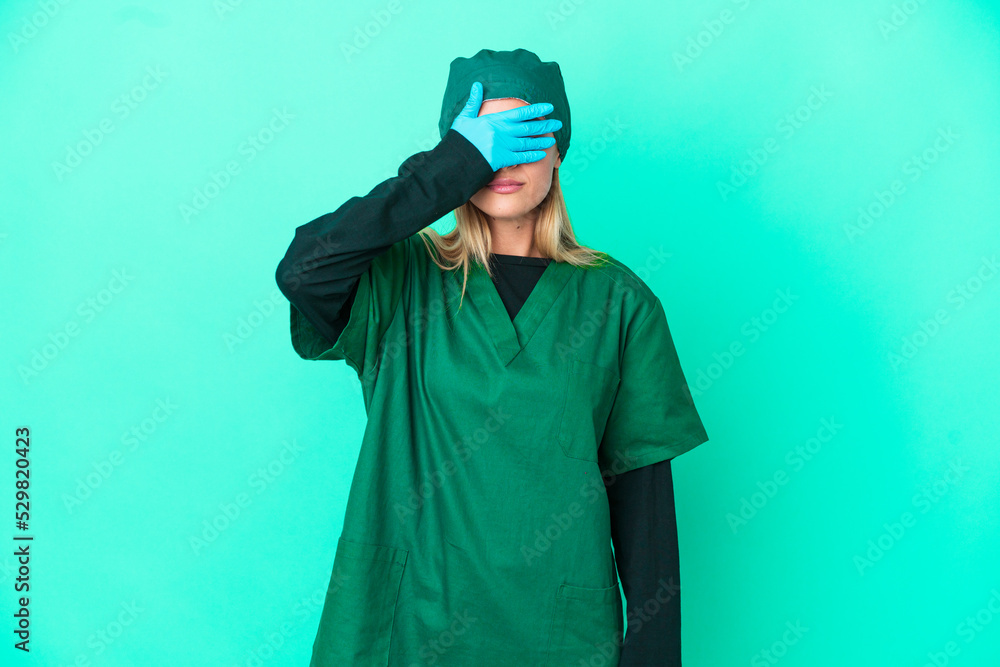 Young surgeon Uruguayan woman in green uniform isolated on blue background covering eyes by hands. Do not want to see something Young surgeon Uruguayan woman in green uniform isolated on blue background covering eyes by hands. Do not want to see something