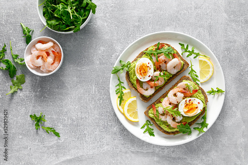 Toast with shrimps, avocado guacamole, arugula and boiled egg, top view