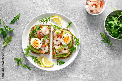 Toast with shrimps, avocado guacamole, arugula and boiled egg, top view