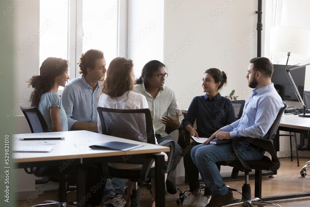 Indian diverse business team employee talking to coworkers, discussing project, telling, explaining ideas. Addicted man speaking, sharing problem on group therapy meeting