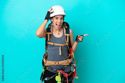 Young Italian rock-climber woman isolated on blue background surprised and pointing finger to the side © luismolinero