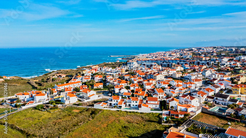 Aerial view of a small European town against blue sky and Atlantic Ocean. Drone view of a beautiful European city with a hilly landscape on ocean background. Beautiful natural landscape. Portugal. © Valua Vitaly