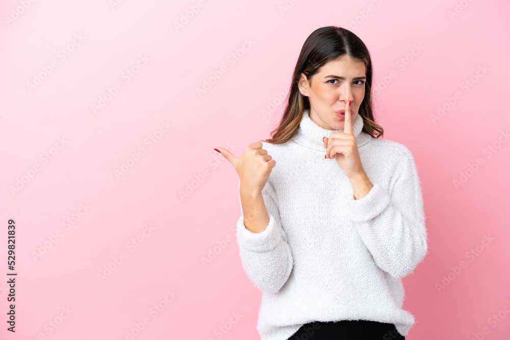 Young Italian woman isolated on pink background pointing to the side and doing silence gesture Young Italian woman isolated on pink background pointing to the side and doing silence gesture