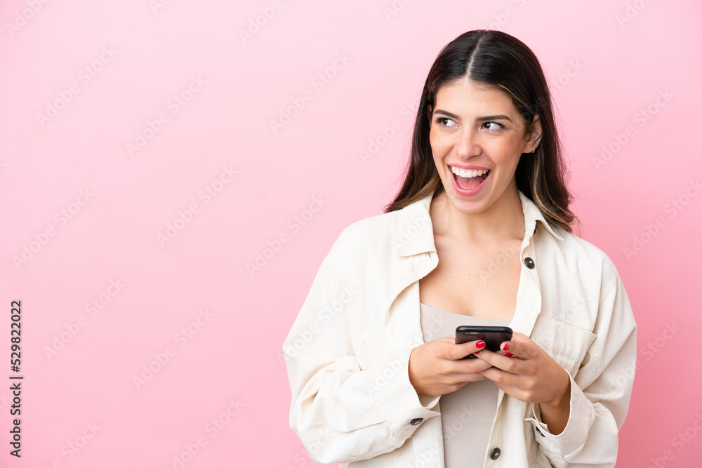 Young Italian woman isolated on pink background using mobile phone and looking up Young Italian woman isolated on pink background using mobile phone and looking up
