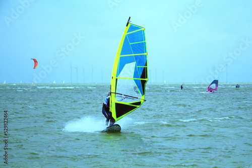 Female windsurfer jibing at IJsselmeer with sailing boats and wind turbines in background, Workum, Netherlands
