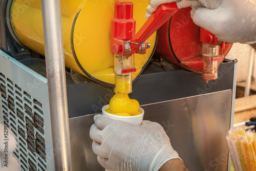 Seller pours frozen juice or serbet into a once-only glass from the machine. Close-up