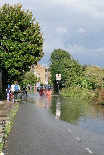 London, England, UK. 10th Sep 2022. Adults and kids ciclysts blocked on kerb wondering how to cross the road as water floods the Thames riverbank after recent thunderstorms photo