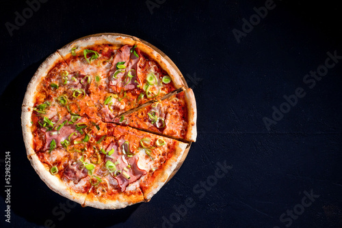 Delicious pizza with mozzarella cheese, ham, leeks on a tomato base on black background. Copy Space