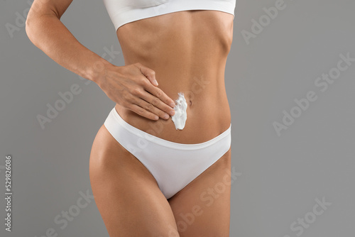 Unrecognizable young female in white underwear applying moisturising body lotion on belly