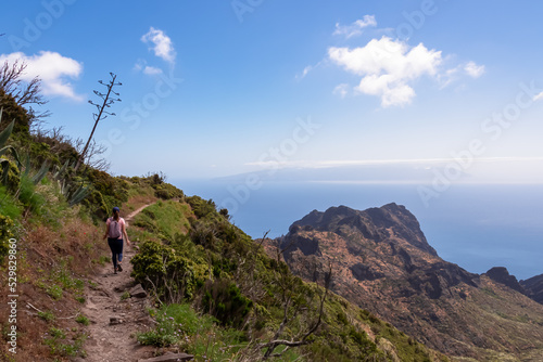 Rear view on backpacking woman on coastal scenic hiking trail near Masca in Teno mountain massif, Tenerife, Canary Islands, Spain, Europe. Fields of agave flowers and cactus plants along the way. Awe