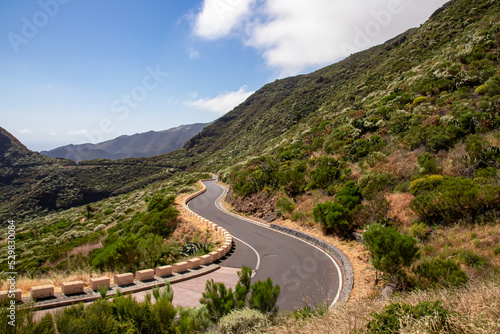 Panoramic view on empty narrow winding curvy mountain road going to remote village Masca, Teno mountain massif, Tenerife, Canary Islands, Spain, Europe. Roadway over hilly terrain with shrub fauna