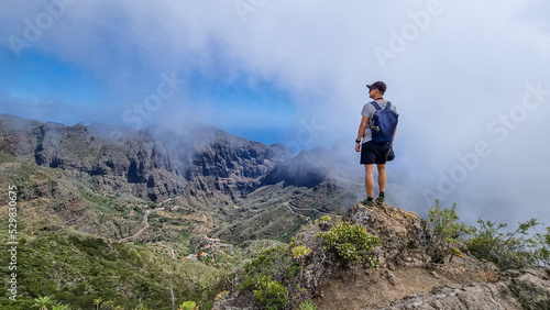 Man with backpack enjoying view on Teno mountain range near Masca village  Tenerife  Canary Islands  Spain  Europe. Fog going down the valley creates a mystical atmosphere. Remote hiking trail