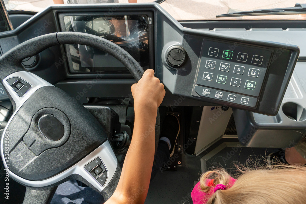 A close-up of a child's hand on the steering wheel of a bus. A child inside the cab of a car. View of the steering wheel and dashboard of a new modern bus. Urban public transport