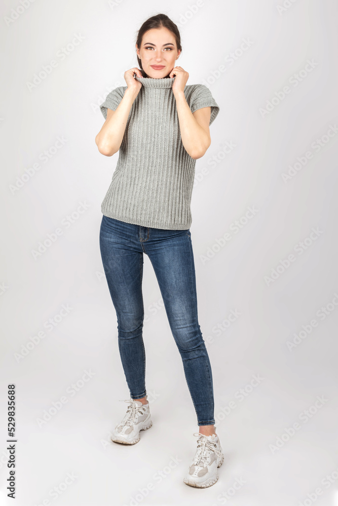Fashion and make-up concept. Studio portrait of beautiful and sexy brunette woman with beautiful body shape wearing gray sweater without sleeves and jeans Fashion and make-up concept. Studio portrait of beautiful and sexy brunette woman with beautiful body shape wearing gray sweater without sleeves and jeans