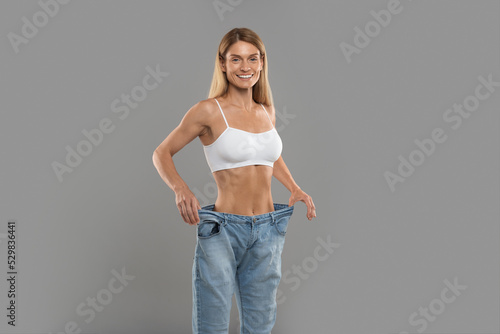 Beautiful Slim Woman In Oversized Jeans Standing Over Grey Studio Background