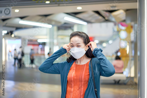 Asian Woman was wearing and putting white face mask on her face in shopping mall.