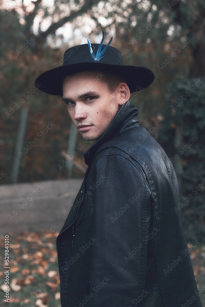 Portrait of man in black hat with blue feather and jacket near autumn evening Portrait of man in black hat with blue feather and jacket near autumn evening