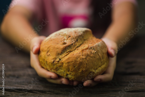 Cinematic macro shot of professional artisan baker is showing in camera just prepared fresh whole grains white bread taken out of oven in rustic bakery kitchen. photo