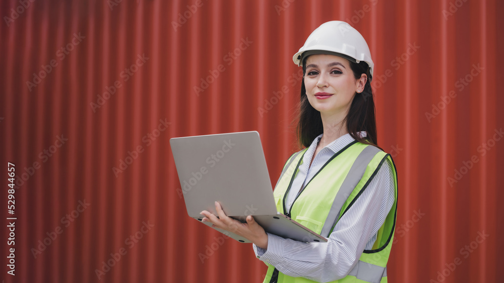 Portrait Caucasian woman with Container box Shipping Logistics Engineering of Import/Export Transportation Industry, Female Safety Transport Engineer holding laptop standing confidently at shipyard.