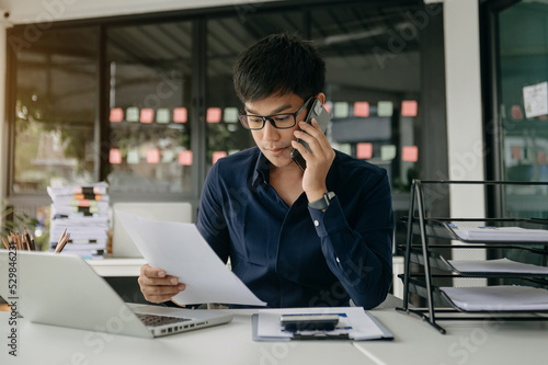 Business asian man Talking on the phone and using a laptop with a smile while sitting at office..