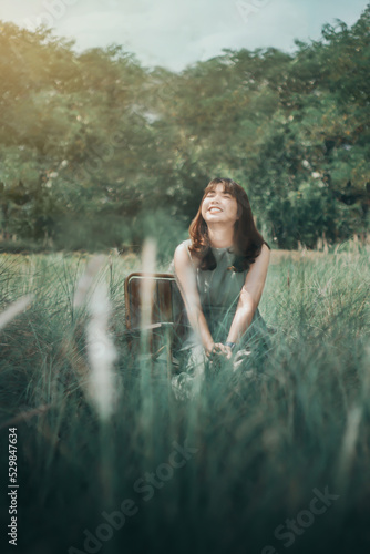 Young asian black hair woman in green dress smiling chin up sitting among meadow closed eye and feeling fresh. Portrait of woman in summer with grass field.