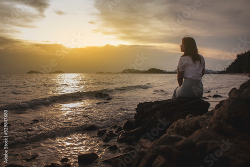 Silhouette of long hair woman sit on the stone beside the beach and wave at sunset sunrise © Rattanapon