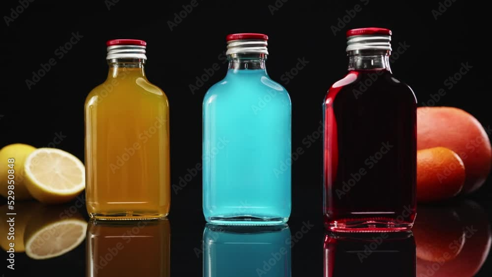 colorful drinks in glass bottles rotating on a table splashed with water colorful drinks in glass bottles rotating on a table splashed with water