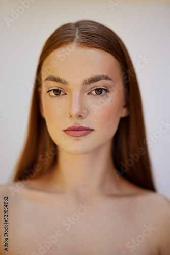 Beauty photoshoot. Female model with red hair, brown eyes, freckles, clear skin, against a white background. 
