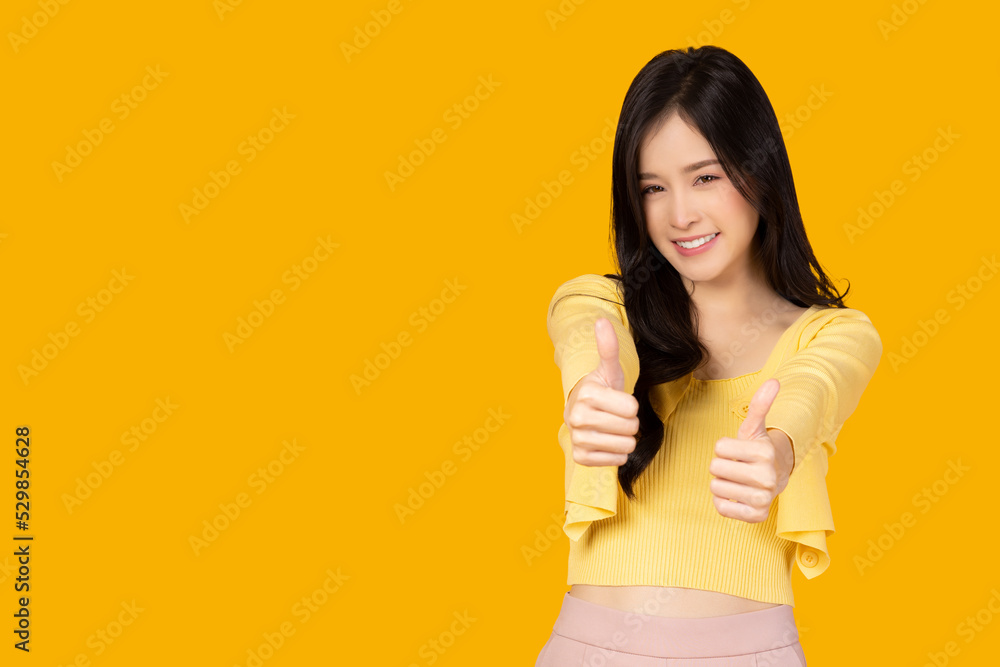 Smiling beautiful Asian woman showing thumbs up isolated on yellow ...