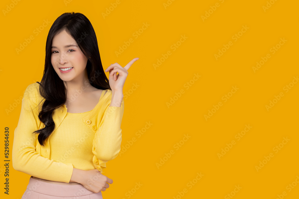 Beautiful young Asian woman pointing up to copy space and looking at camera with smile face and happy Pretty girl act like a satisfied product, use for advertising with isolated on yellow background Beautiful young Asian woman pointing up to copy space and looking at camera with smile face and happy Pretty girl act like a satisfied product, use for advertising with isolated on yellow background