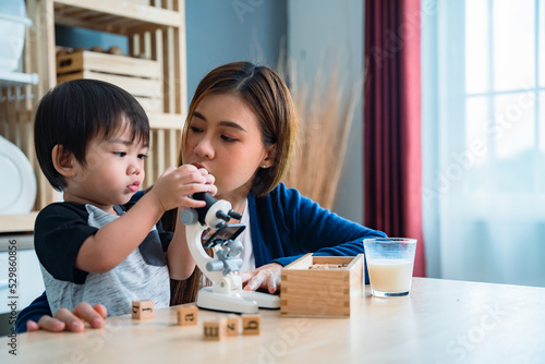 Asian baby boy playing microscope toys with his mother sitting beside.