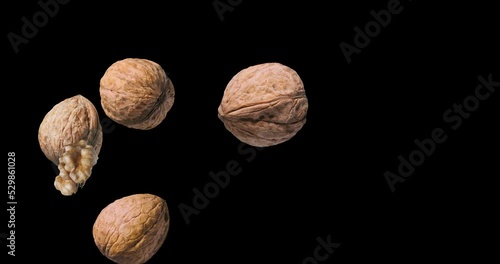 Three walnuts and two shelled walnuts rotate slowly on a black background. 