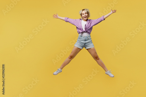 Full body young overjoyed excited fun cool blonde woman 20s she wears pink tied shirt white t-shirt jump high with outstretched hands legs isolated on plain yellow background eople lifestyle concept © ViDi Studio