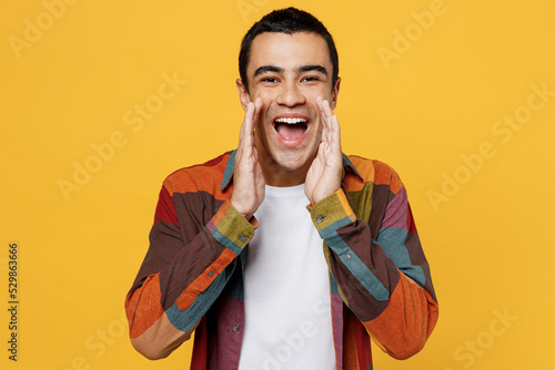 Slika na platnu Young promoter middle eastern man 20s he wear casual shirt white t-shirt scream hot news about sales discount with hands near mouth isolated on plain yellow background studio People lifestyle concept