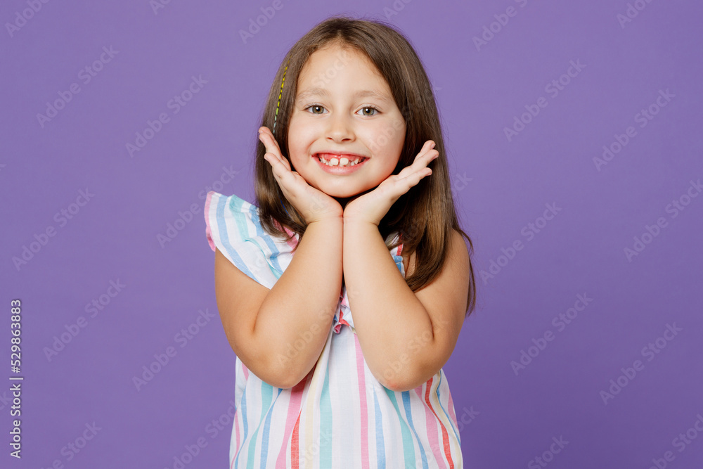Little smiling nice cheerful happy european fun kid child girl 5-6 years old wears striped dress hold face isolated on plain pastel light purple background. Mother's Day love family lifestyle concept. Little smiling nice cheerful happy european fun kid child girl 5-6 years old wears striped dress hold face isolated on plain pastel light purple background. Mother's Day love family lifestyle concept.
