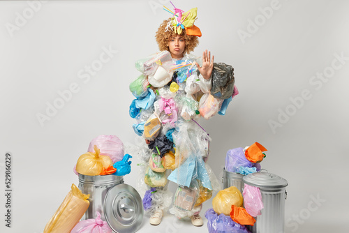 Fotografi Full length shot of angry female activist has strict expression makes stop gesture demands from people being ecologically friendly surrounded by much litter poses indoor