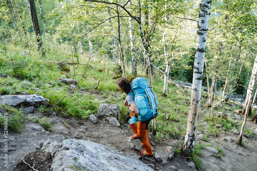 A man carries a large backpack of equipment, mountain Sherpas walk along the mountainside, a taiga path, a birch forest, a guy drags a bag, a stone road.
