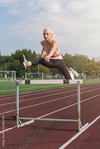 Young woman athlete runnner running hurdles at the stadium outdoors