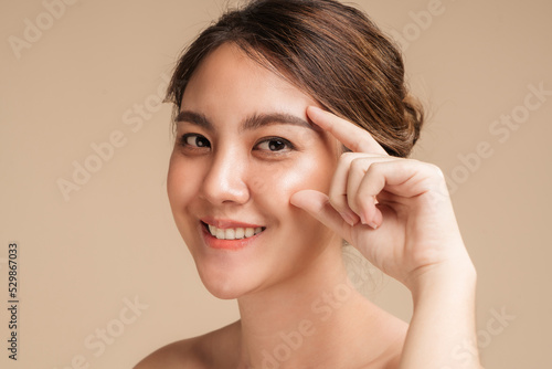 Closeup photo of a smiling brunette asian woman touching her eyes with natural makeup, hydrated skin, Facial face and wrinkles treatment concept.
