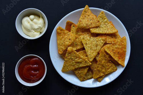 Delicious peppery nachos on a plate with sauces on a black background. Delicious snack with corn nachos close-up.