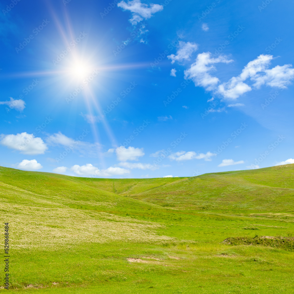 Obraz premium Vast grassy meadow with distant hills and sun on sky.