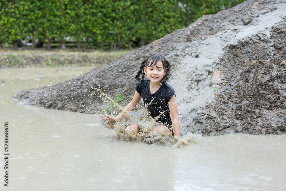 Happy child girl playing in large wet mud and dirt in rainy season Happy child girl playing in large wet mud and dirt in rainy season
