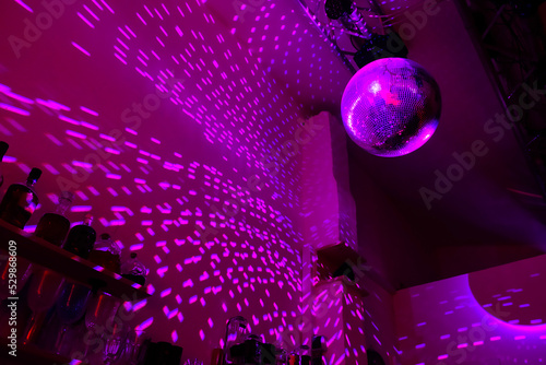 Disco ball reflecting the light of pink-purple color in a dark hall for discos. 