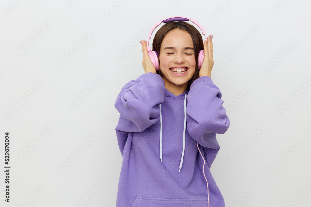a cheerful, happy woman in a purple tracksuit enjoys music with her eyes closed, holding the headphones with her hands on both sides, smiling pleasantly. Studio Photography a cheerful, happy woman in a purple tracksuit enjoys music with her eyes closed, holding the headphones with her hands on both sides, smiling pleasantly. Studio Photography