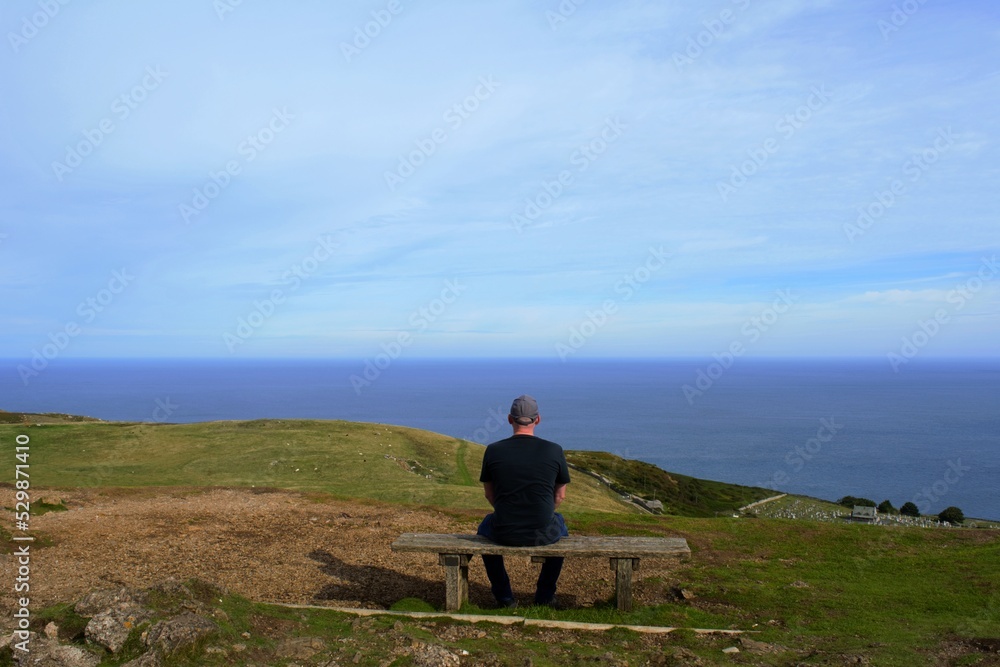 person sitting on a bench looking out to sea person sitting on a bench looking out to sea